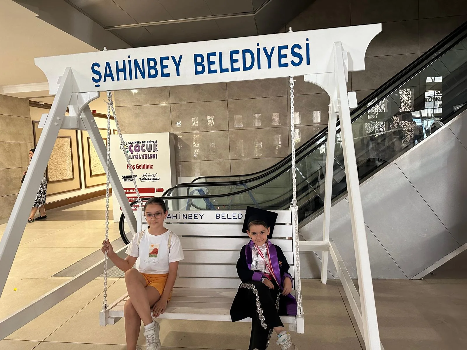 Beyaz salıncakta yan yana oturan Defne ve Demir